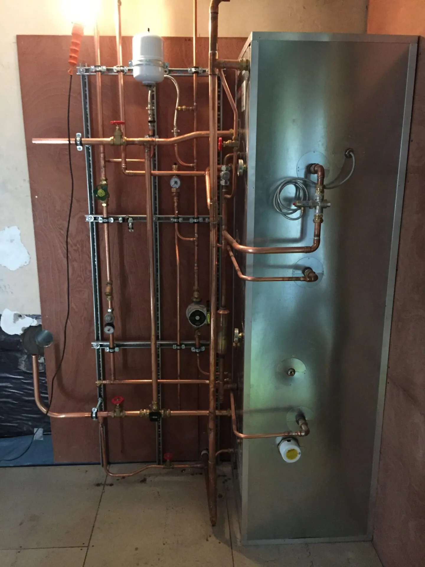 A rectangular thermal store in a plant room, with copper pipework, a pump and an expansion vessel beside it