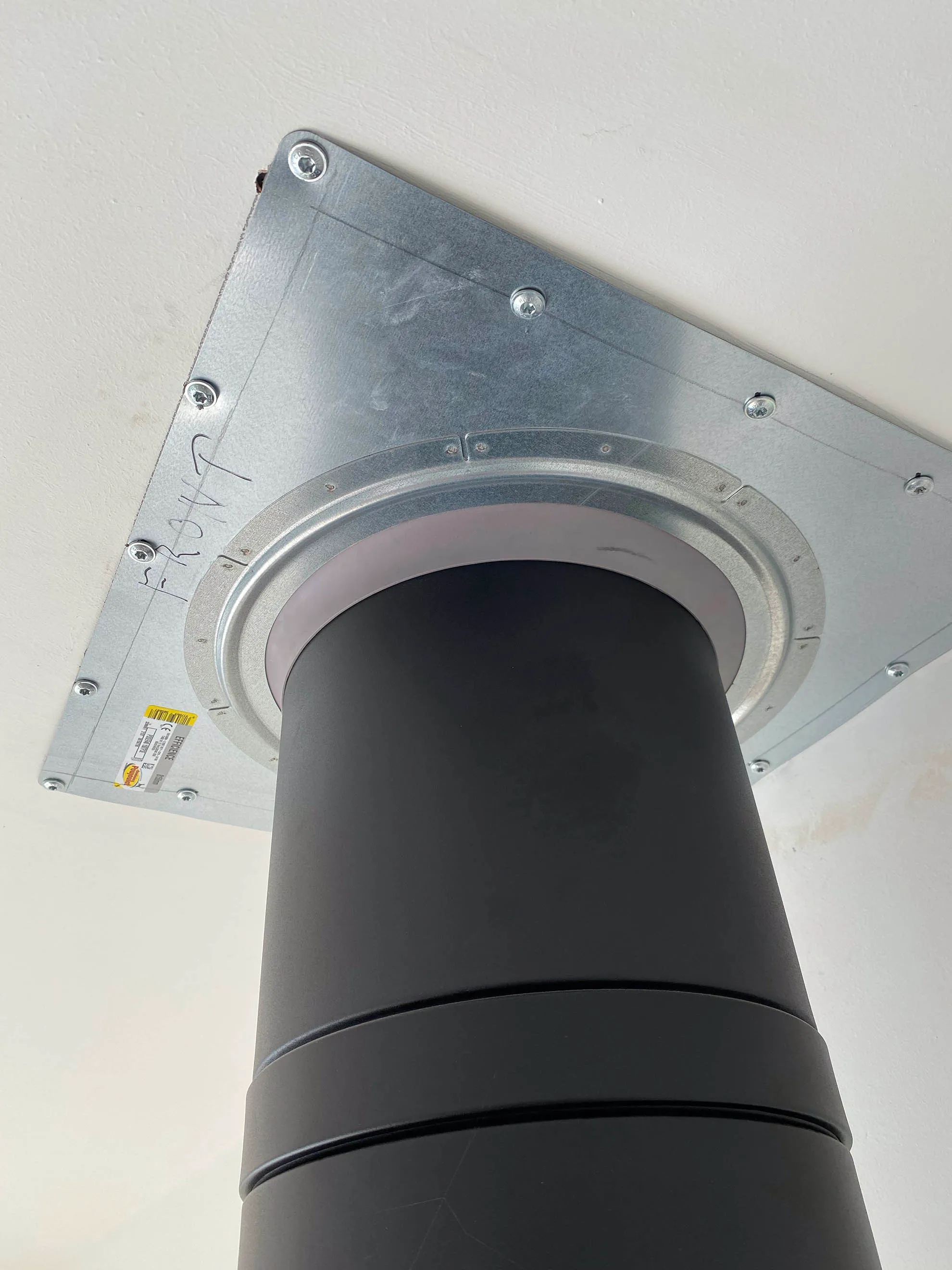 A twin-wall flue passing through a steel ceiling plate, seen from below