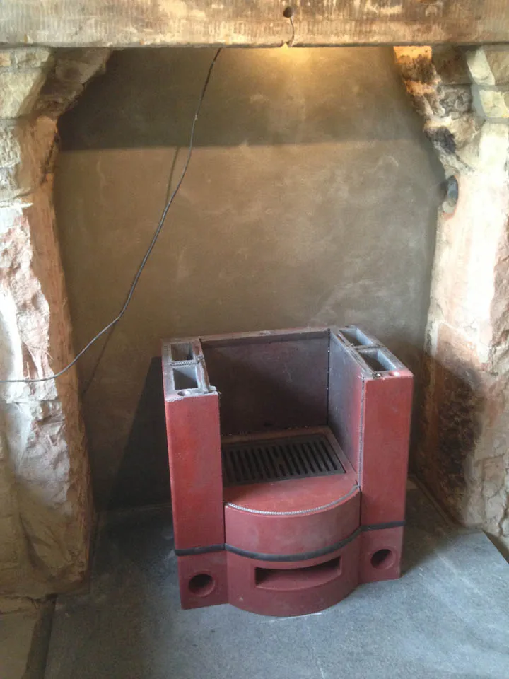 A red cast-iron stove base standing in a bare stone fireplace opening before installation