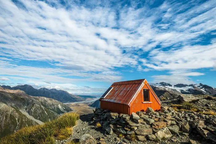 A corrugated orange mountain hut with a solar panel on its roof, above a glacial valley