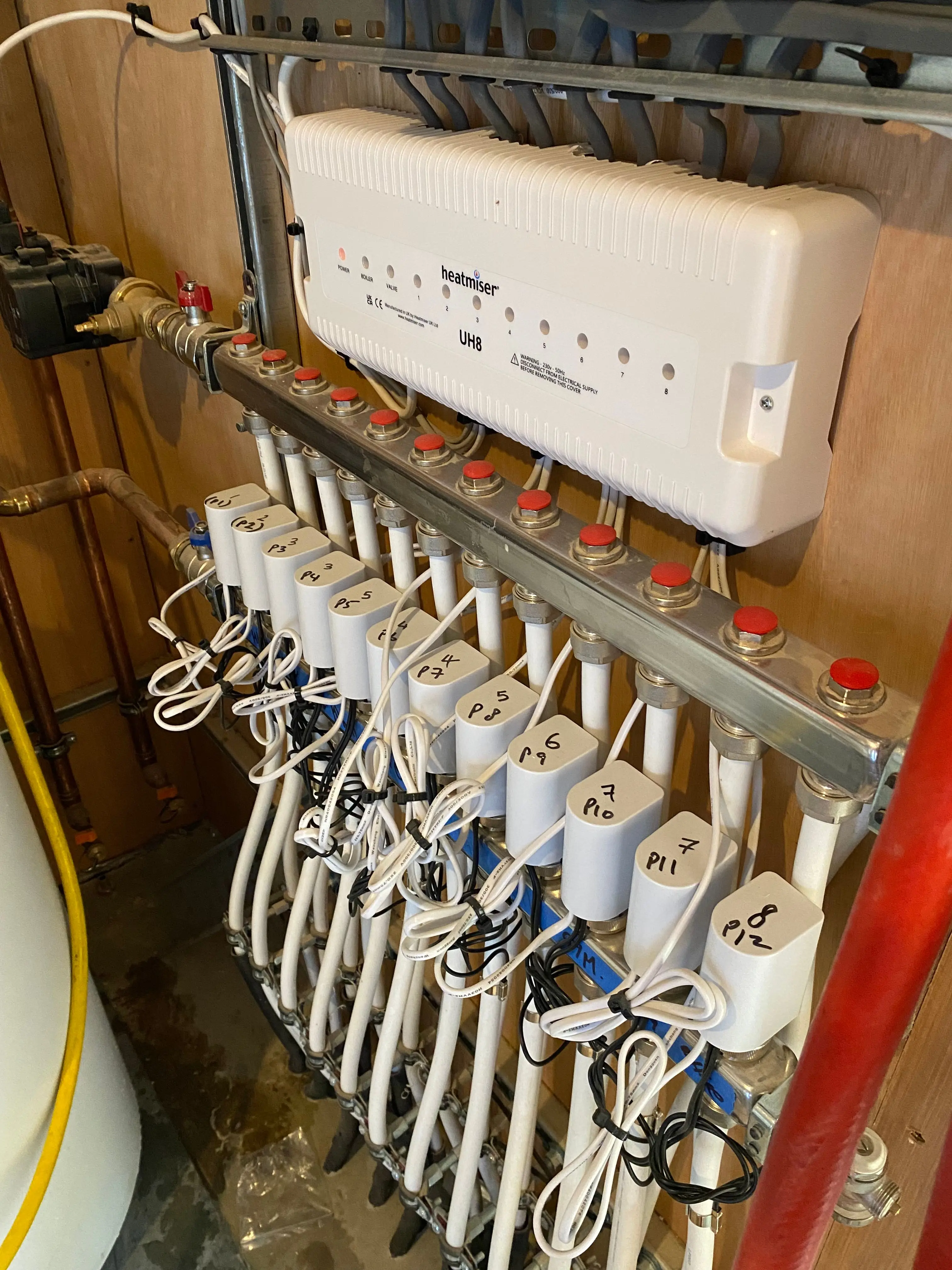 A twelve-loop underfloor manifold, each circuit labelled, under a Heatmiser UH8 wiring centre