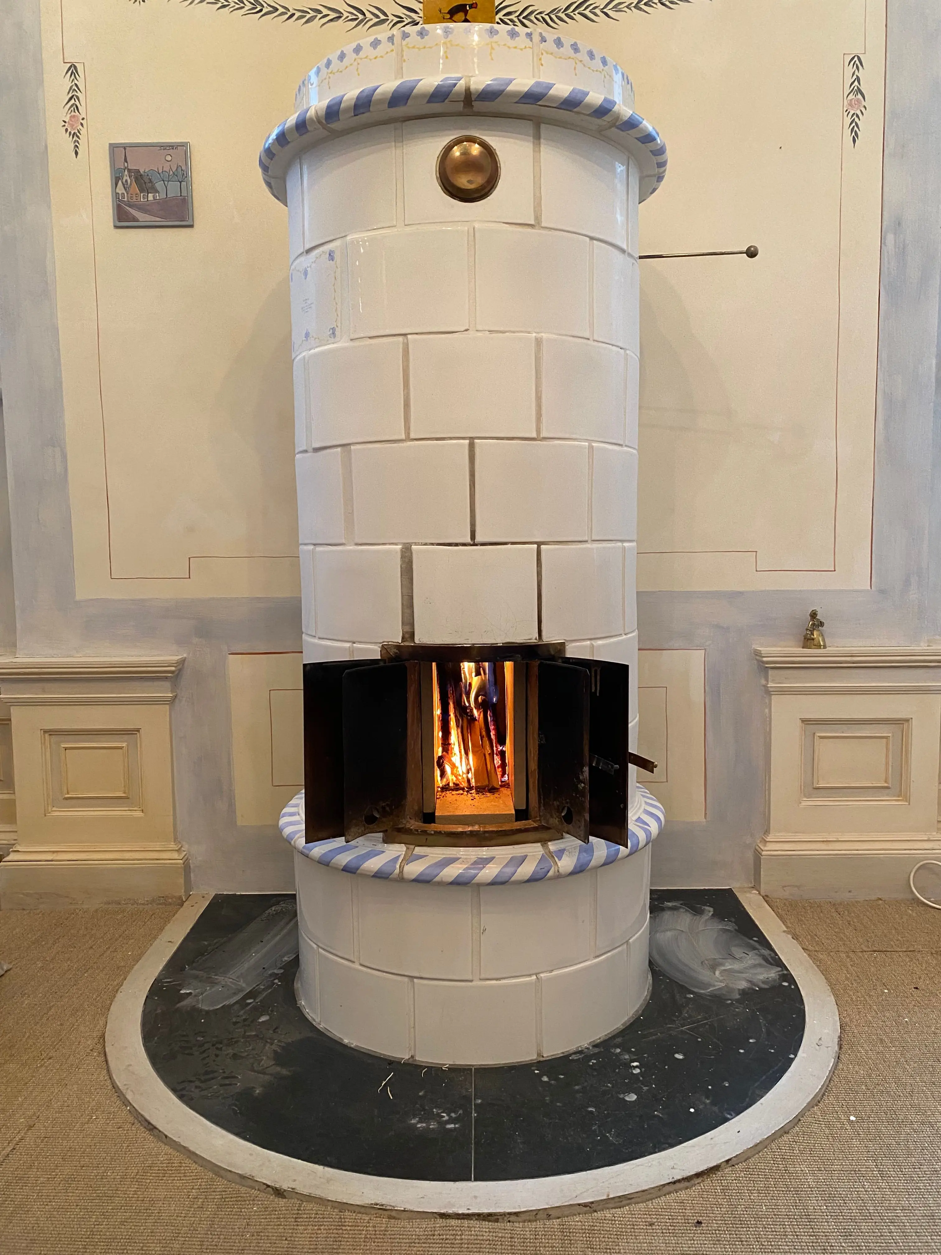 A refurbished antique tile stove alight, white with blue-and-white banding, in a hand-painted room